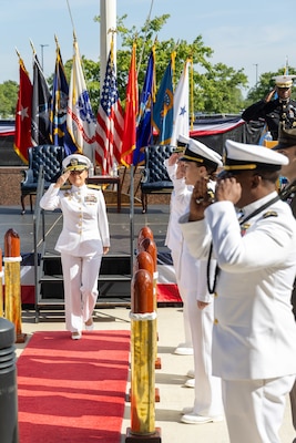 A woman in a white dress Navy uniform marches off stage in between people in uniform.