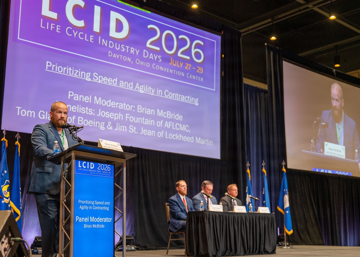 A moderator at a podium and a table with panel members on a stage.
