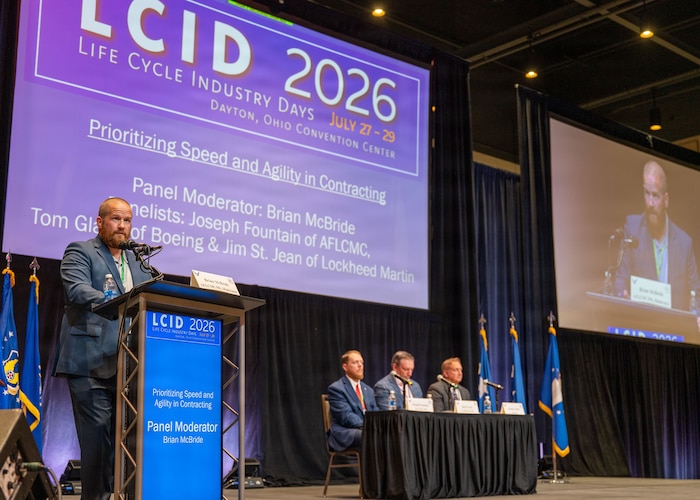 A moderator at a podium and a table with panel members on a stage.