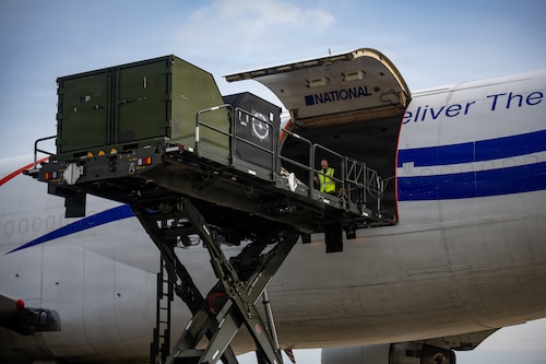 Filipe Antunes, National Airlines loadmaster, directs an aircraft cargo loader and transporter towards a Boeing 747 transport aircraft in support of Red Flag-Alaska 26-3.