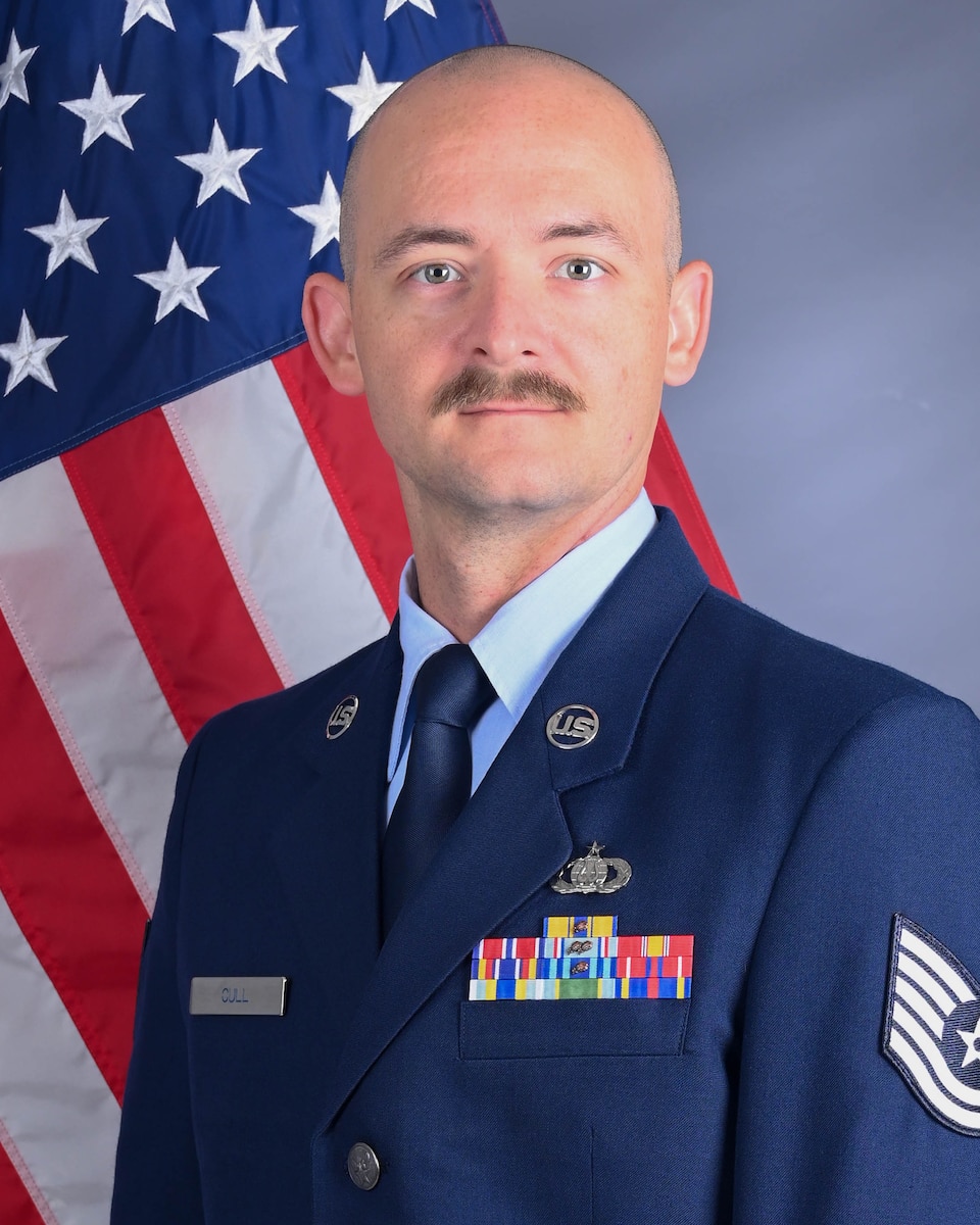 Official photo of TSgt Levi Cull in front of the American flag. He is wearing his blue service dress uniform