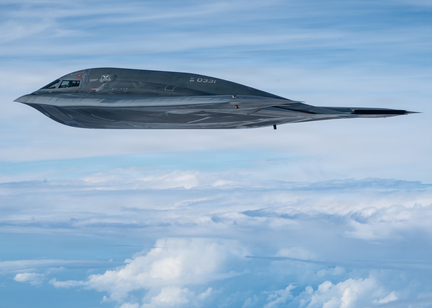 B-2 Bomber flying (nose facing left), surrounded by blue sky