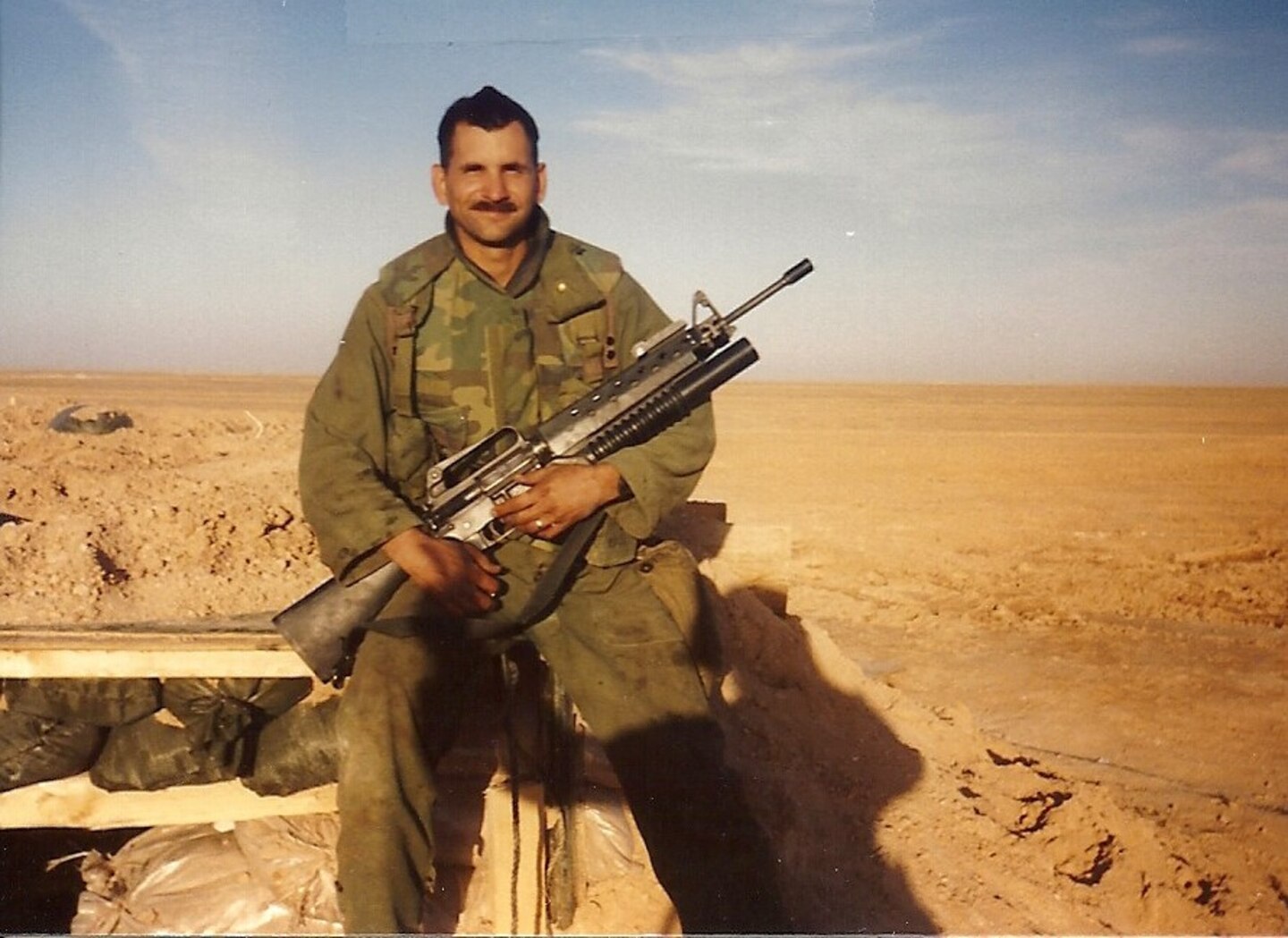 Man holding weapon in desert.