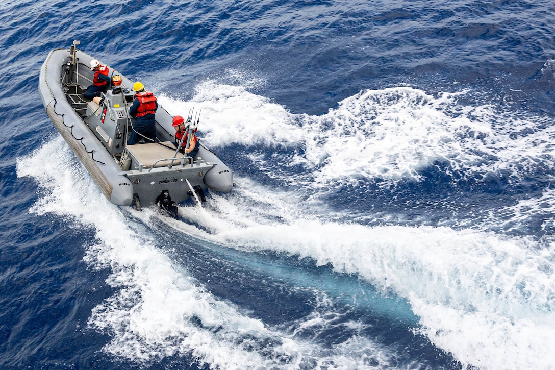 Four sailors wearing life vests and hard hats operate a small boat in a body of water during the day.