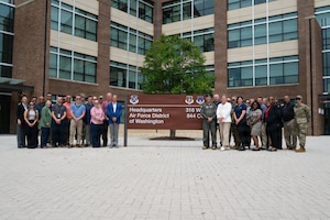 A group of adults stand in front of sign for a picture.