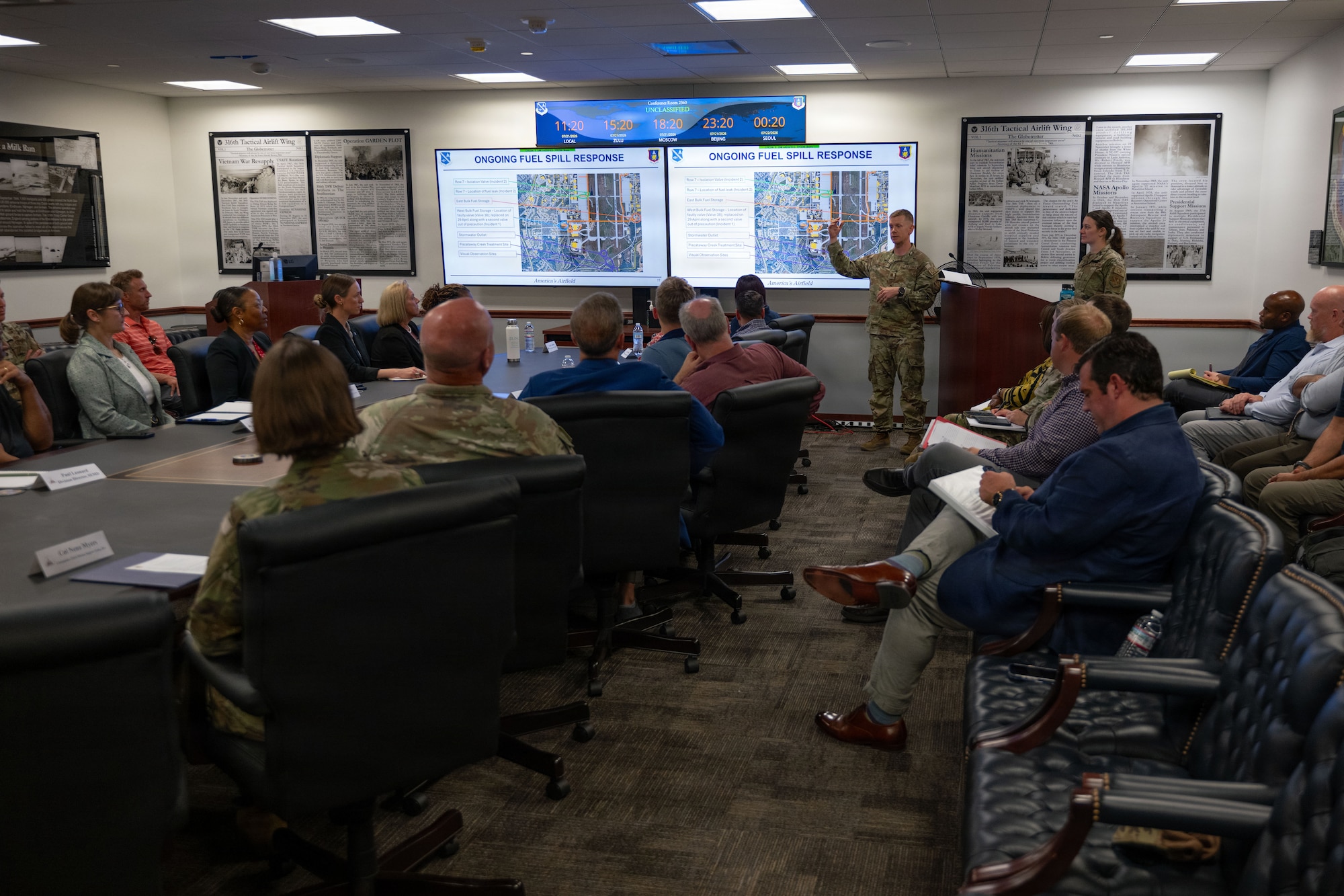 A man in OCP's stands in the front of a conference room and speaks to a group of seated adults.