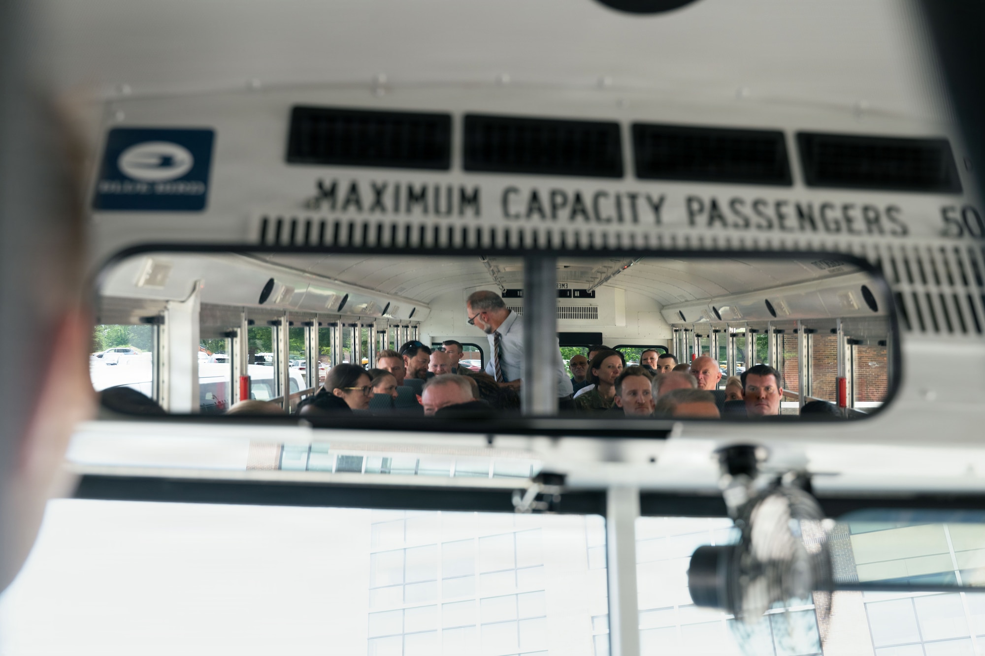 Inside a rearview mirror we see a group of people sitting on a bus.