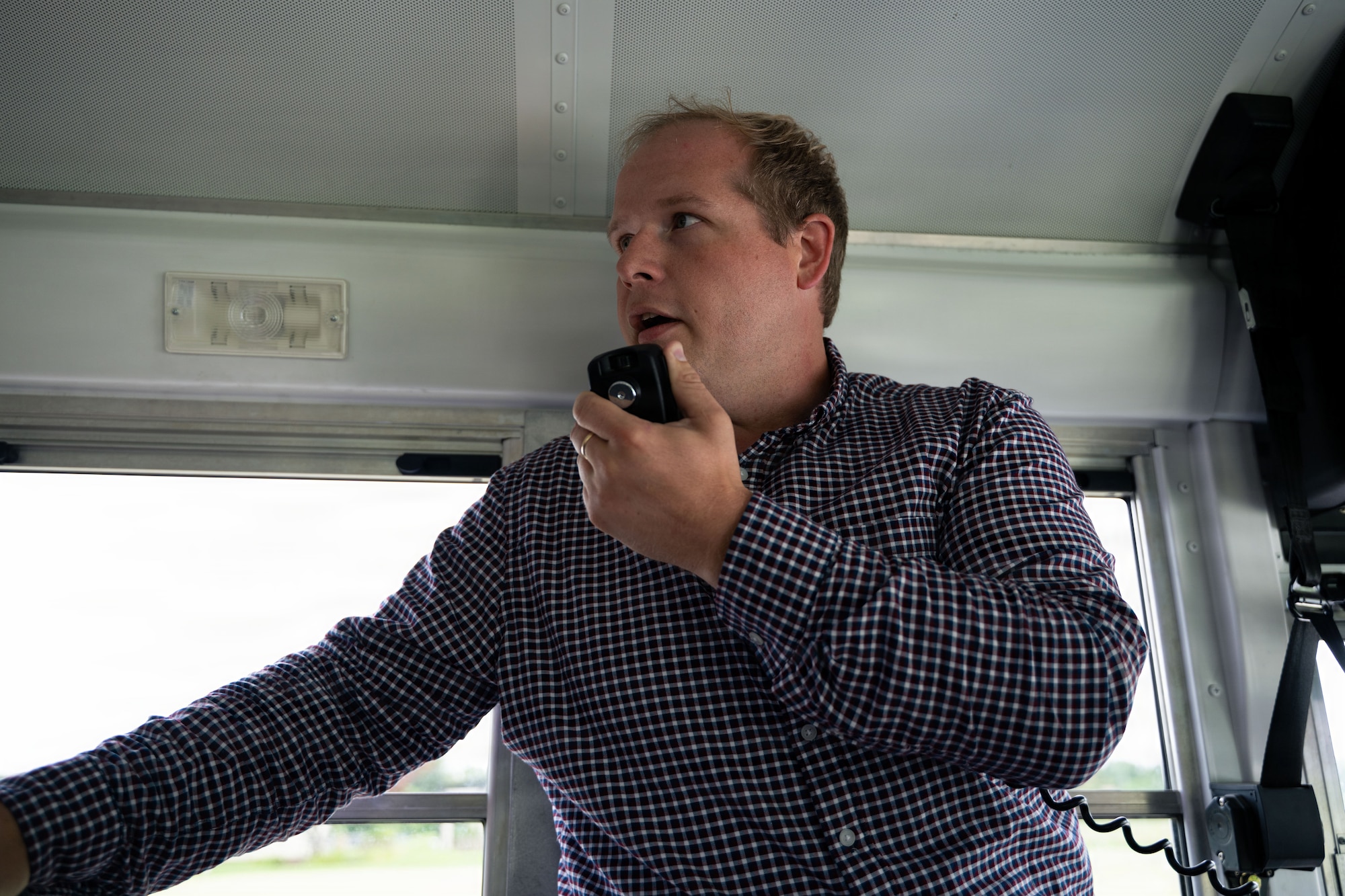 A man stands at the front of a bus and speaks into an intercom system.