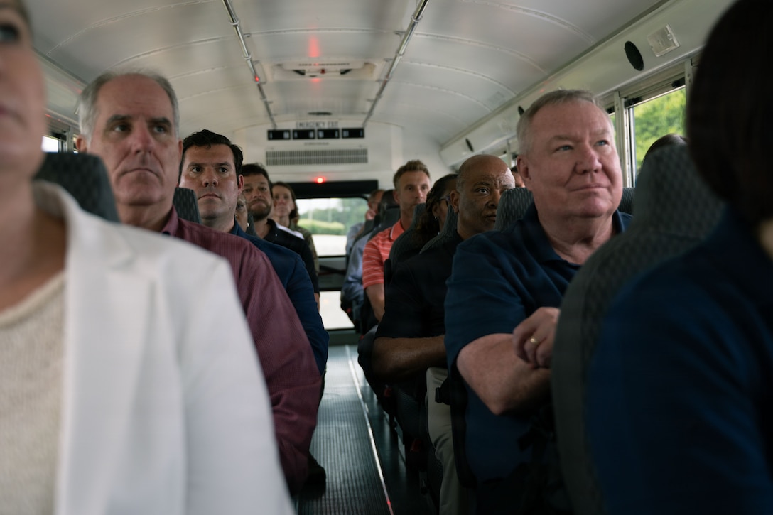 Adults sit inside a bus and look up at a man talking.
