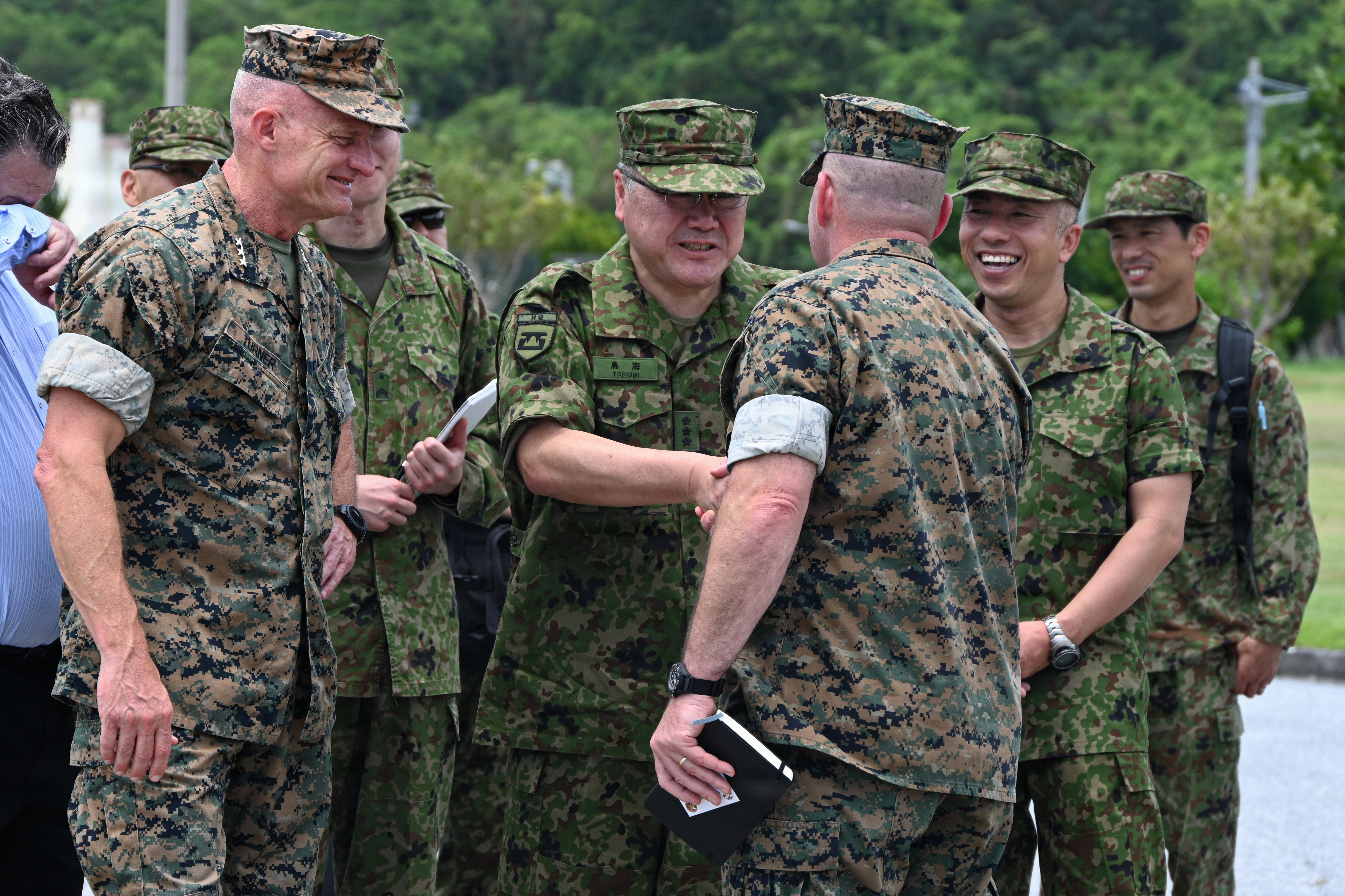 Japan Ground Self-Defense Force Lt. Gen. Seiji Toriumi, center, commanding general of Western Army, and U.S. Marine Corps Lt. Gen. Roger Turner, left, Commanding General of III Marine Expeditionary Force, greet Brig. Gen. Christopher Haar, commanding general of 3rd Marine Logistics Group, during Valiant Shield 26 at White Beach, Okinawa, Japan, June 29, 2026. Toriumi, Turner, and Haar viewed the testing and operating of the Foam Raiding Craft created in part by Marines with Intermediate Repair Company, 3rd Maintenance Battalion, 3rd MLG, as part of Resilient Advanced Manufacturing for Contested Environments, or RAMFORCE, an initiative hosted by the Office of the Under Secretary of Defense for Research and Engineering. The innovative event brought together military personnel, government laboratories, and private industry to evaluate how advanced manufacturing technologies could enable expeditionary forces to repair, replace and even produce critical equipment at the point of need. (U.S. Marine Corps photo by Cpl. Rachel Mason)