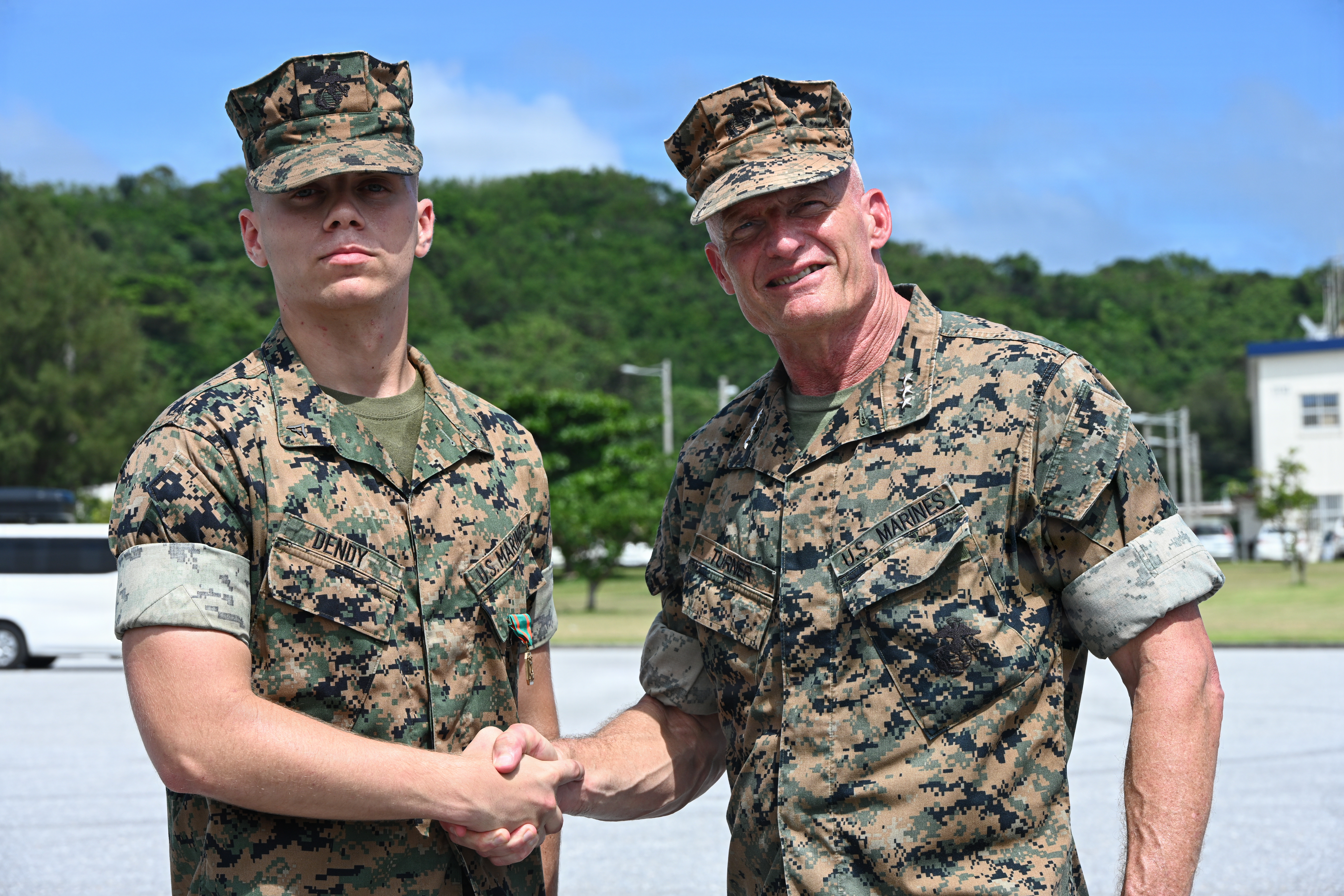 U.S. Marine Corps Lance Cpl. Jesse Dendy, an amphibious combat vehicle technician with Intermediate Repair Company, 3rd Maintenance Battalion, 3rd Marine Logistics Group, shakes hands with Lt. Gen. Roger Turner, Commanding General of III Marine Expeditionary Force, after receiving a Navy and Marine Corps Achievement Medal during Valiant Shield 26 at White Beach, Okinawa, Japan, June 29, 2026. Intermediate Repair Company participated in Resilient Advanced Manufacturing for Contested Environments, or RAMFORCE, an initiative hosted by the Office of the Under Secretary of Defense for Research and Engineering. The innovative event brought together military personnel, government laboratories and private industry to evaluate how advanced manufacturing technologies could enable expeditionary forces to repair, replace and even produce critical equipment at the point of need. (U.S. Marine Corps photo by Cpl. Rachel Mason)