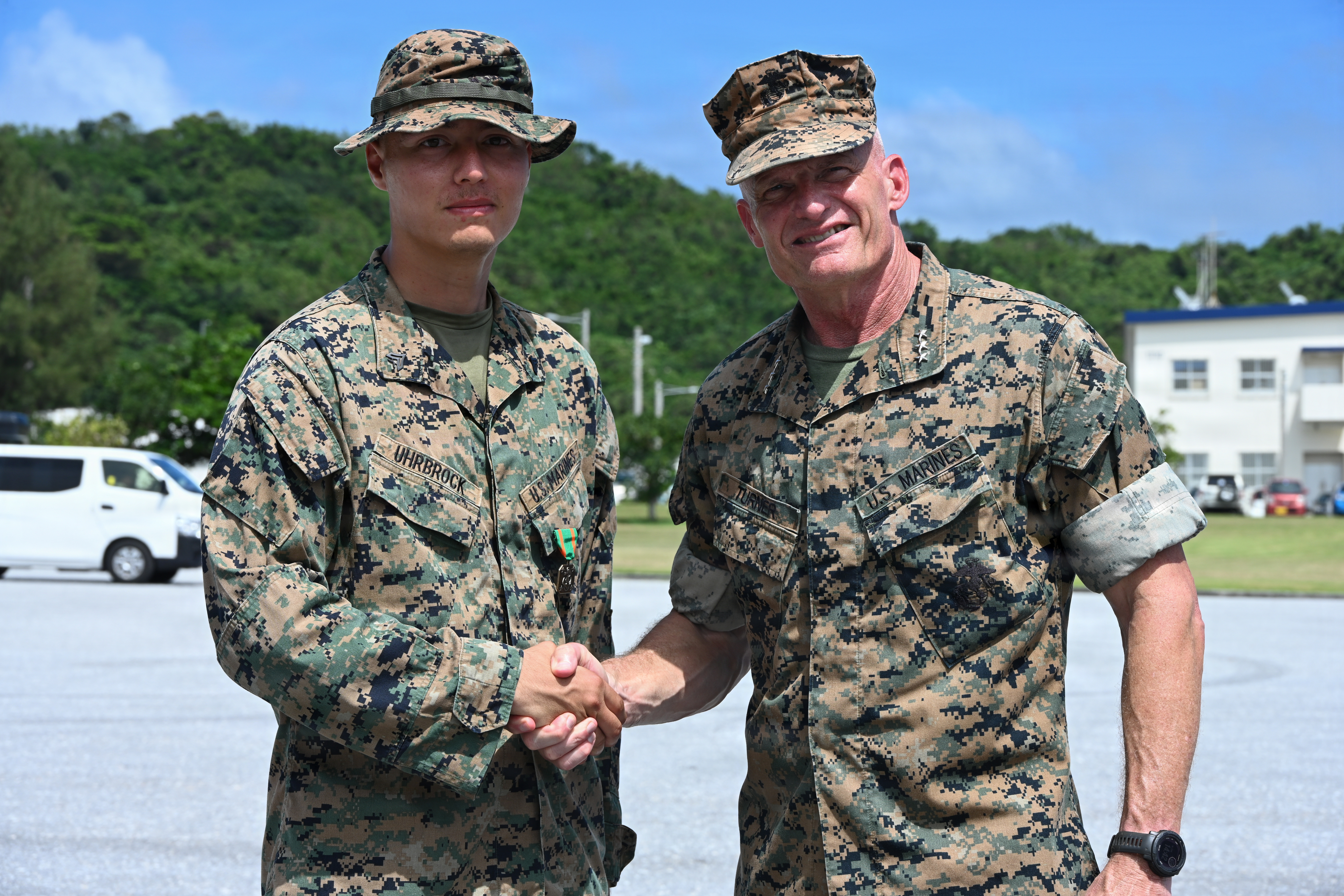 U.S. Marine Corps Cpl. Noah Uhrbrock, left, a calibration technician with Intermediate Repair Company, 3rd Maintenance Battalion, 3rd Marine Logistics Group, shakes hands with Lt. Gen. Roger Turner, Commanding General of III Marine Expeditionary Force, after receiving a Navy and Marine Corps Achievement Medal during Valiant Shield 26 at White Beach, Okinawa, Japan, June 29, 2026. Intermediate Repair Company participated in Resilient Advanced Manufacturing for Contested Environments, or RAMFORCE, an initiative hosted by the Office of the Under Secretary of Defense for Research and Engineering. The innovative event brought together military personnel, government laboratories and private industry to evaluate how advanced manufacturing technologies could enable expeditionary forces to repair, replace and even produce critical equipment at the point of need. (U.S. Marine Corps photo by Cpl. Rachel Mason)