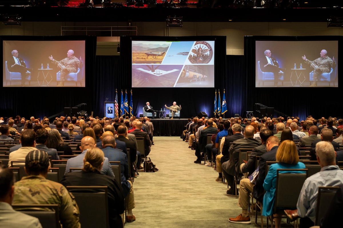 Longview of man on stage speaking in front of large screens showing USAF planes.