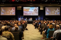 Longview of man on stage speaking in front of large screens showing USAF planes.