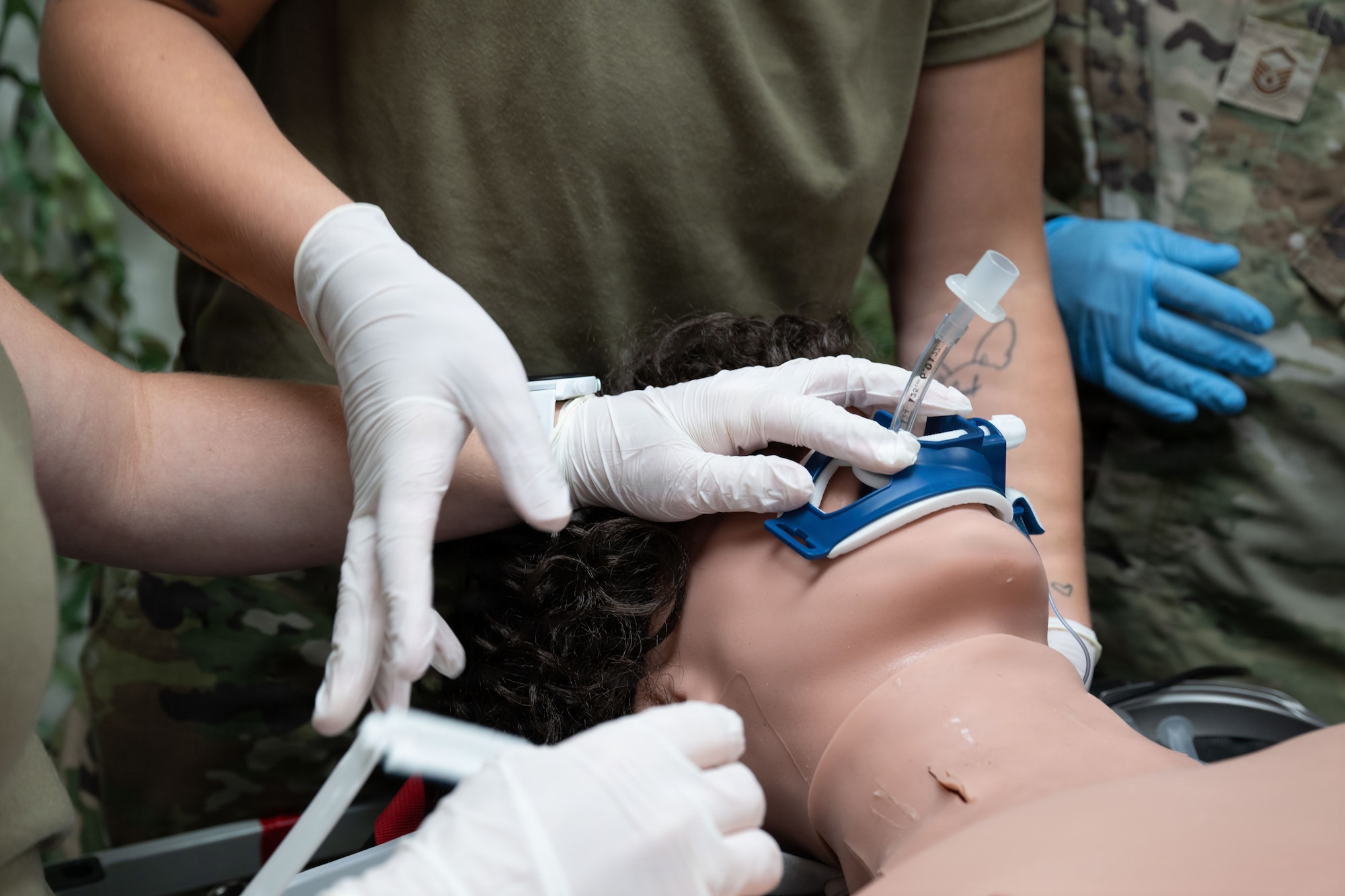 Multiple Airmen's hands on the face of a testing dummy while a video laryngoscopy is performed.