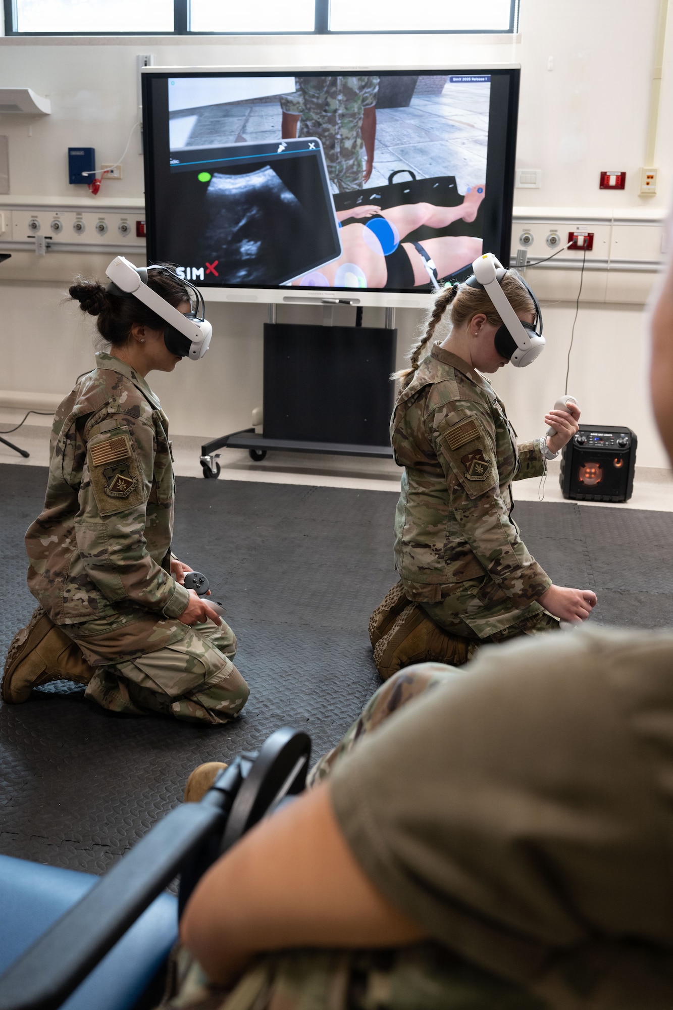 Two Airmen sit on the floor with virtual reality masks on while performing aid to a patient during a virtual reality training.