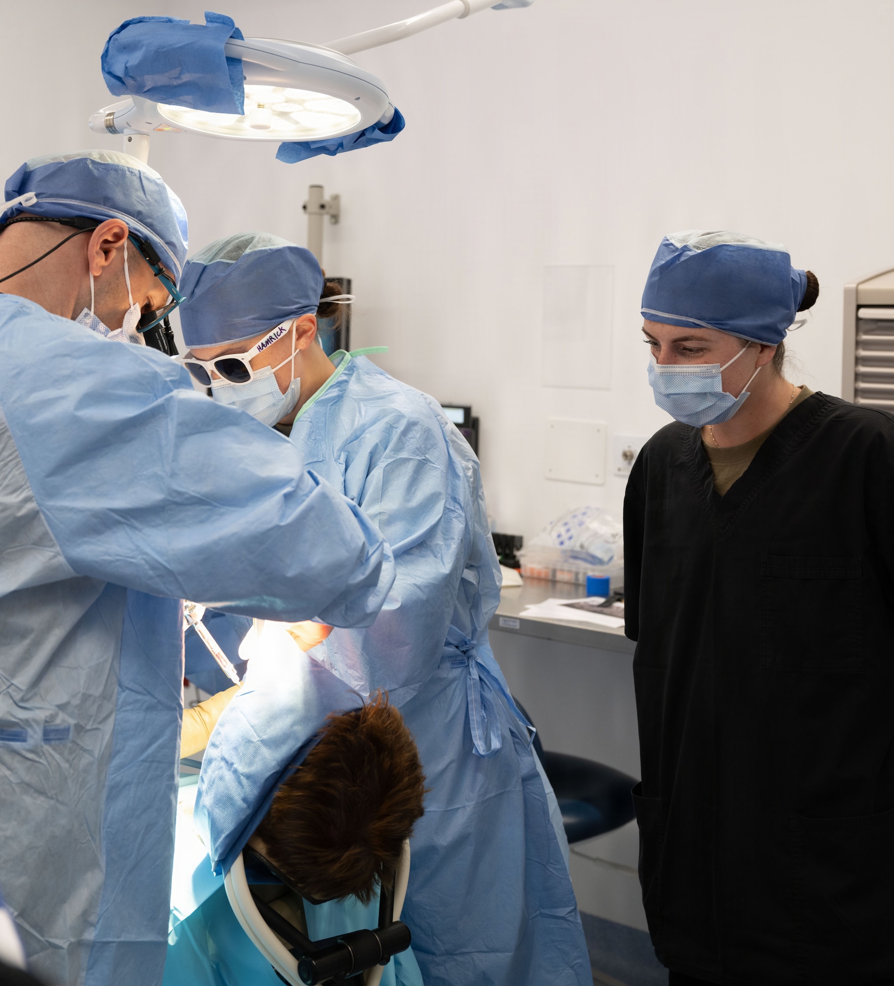 Dentists perform oral surgery on a military member while a training technician overlooks.
