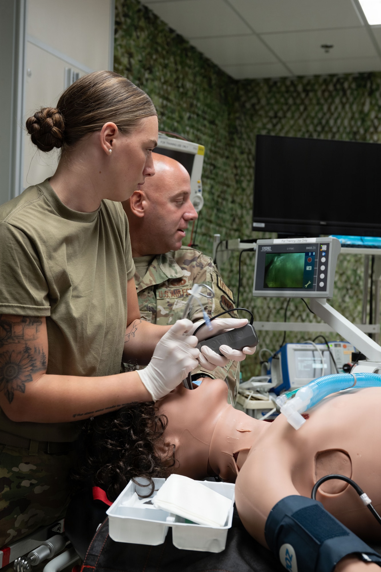 Two people look at a screen while one female military member performs a training laryngoscopy.