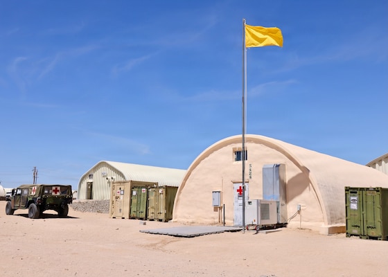 The Consolidated Aid Station (CAS) supports Marines and Sailors during Integrated Training Exercise (ITX) 3-26 at Camp Wilson aboard Marine Air-Ground Task Force Training Command/Marine Corps Air Ground Combat Center Twentynine Palms. A yellow heat condition flag flies outside the facility, indicating environmental conditions for personnel operating in the desert, while a dedicated emergency response vehicle remains staged to rapidly transport injured service members from the training area if needed. ITX is the Marine Forces Reserve's premier live-fire combined arms exercise, preparing Marine Air-Ground Task Forces for operational readiness in realistic combat environments. (U.S. Navy photo by Christopher Jones, NH/NMRTC Twentynine Palms public affairs officer).