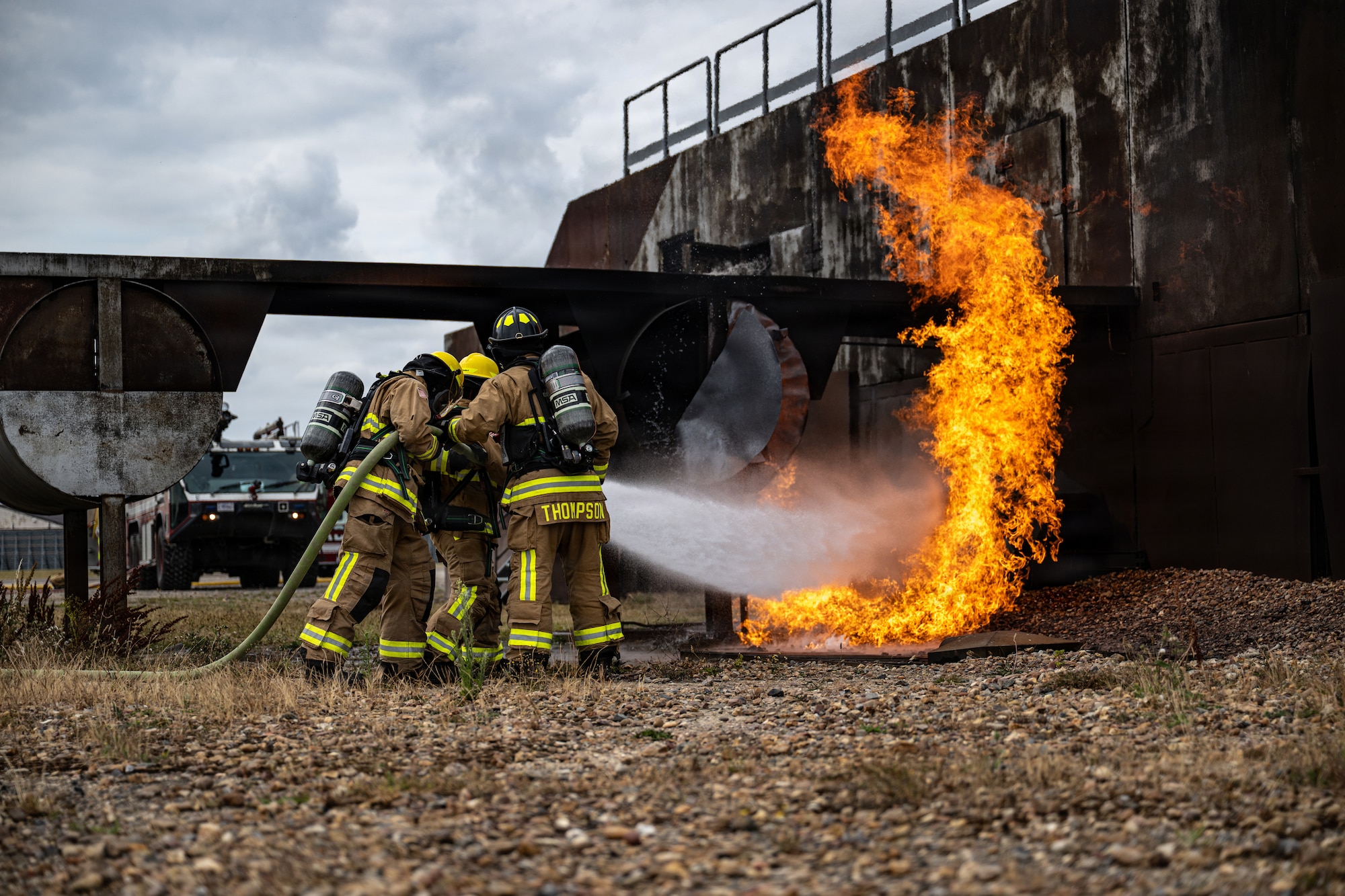 U.S. Air Force Airman 1st Class Andrew Gonzalez, Airman 1st Class Elias Villaseñor, and Senior Airman Jacob Thompson, 100th Civil Engineer Squadron firefighters, extinguish a fire during the 100th CES Fire Department Rookie Academy at RAF Mildenhall, England, July 22, 2026.