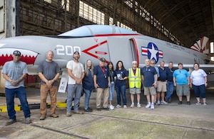 Volunteers who helped in the restoration and transport of the F-4 Phantom II stand in front of the historic military aircraft in Hangar 1 at Joint Base McGuire-Dix-Lakehurst, N.J., July 1, 2026. The restoration project, which took 13 months to complete, was accomplished by a team of 13 volunteers that included Airmen, Sailors, retired veterans, members of the Navy Lakehurst Historical Society and other civilians. (U.S. Air Force photo by Susan Moriarty) (This photo has been altered for security purposes by blurring out identification badges.)