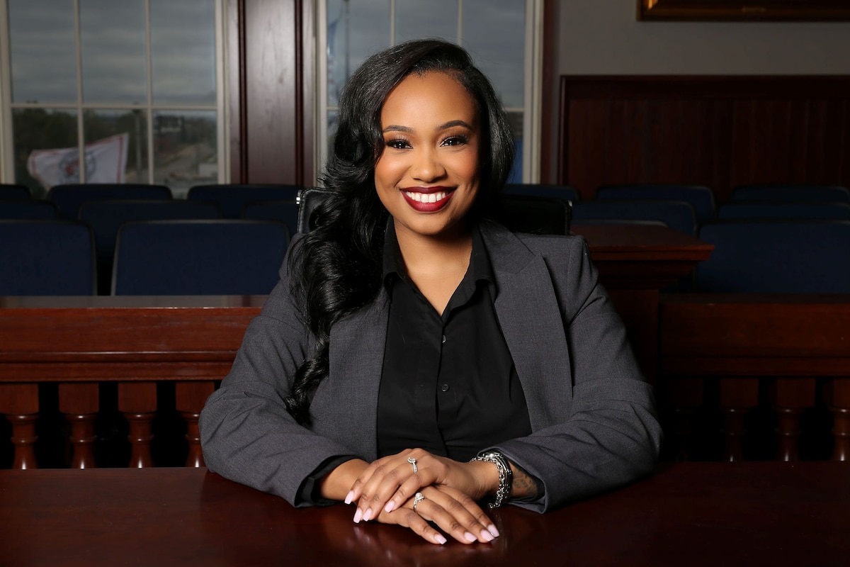 A woman sits at an ornate wooden table in business attire