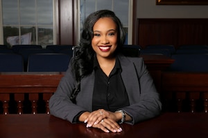 A woman sits at an ornate wooden table in business attire