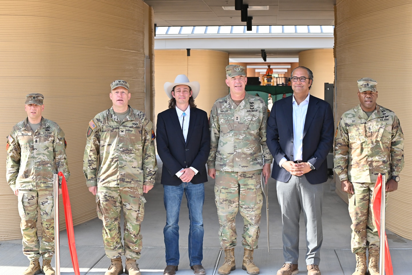A ribbon-cutting ceremony was held at Fort Bliss for the first of 10 3D-printed buildings to be completed for the new Joint Task Force, Southern Border Campus. Pictured from left to right are Command Sgt. Maj. Robert Theus, Fort Bliss Garrison Sergeant Major, Col. Michael Soyka, Fort Bliss Garrison Commander, Jason Ballard, ICON CEO, Maj. Gen Curtis Taylor, Commanding General of the 1st Armored Division and Fort Bliss, Will Hurd, ICON Prime President, and Command Sgt. Maj. Carvet Tate, 1st Armored Division Sergeant Major.
