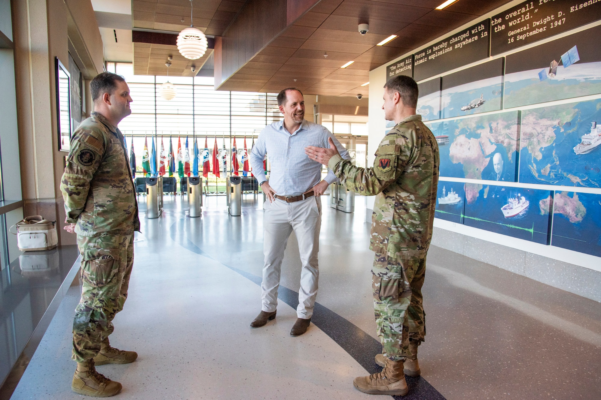 Col. Nicholas DeAngelis (right), briefs Under Secretary of War (I&S) Bradley Hansell (center) about the accomplishments of Staff Sgt. Aaron Jackson (left) at the DoW's sole nuclear treaty monitoring center.  Hansell presented his coin to Jackson for his exceptional grasp of AFTAC's global sensor network and its mission to deliver decision advantage against enduring WMD threats.  (U.S. Air Force photo by Susan A. Romano)
