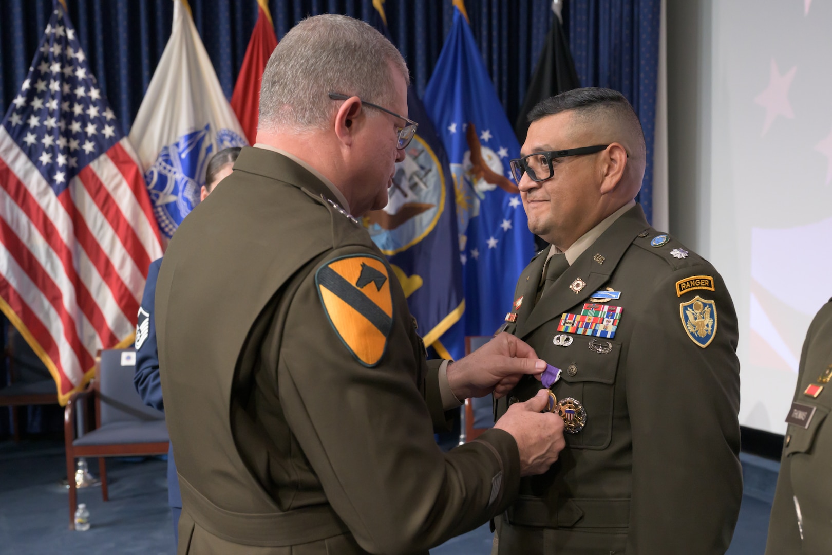 An Army general pins a Purple Heart medal on a male soldier during an awards ceremony.