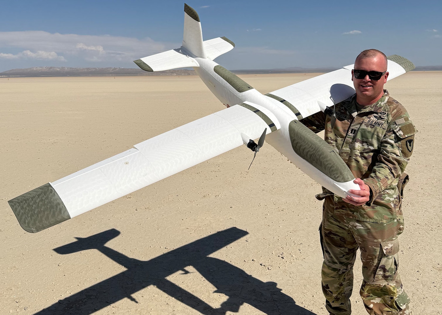 An Army officer holds a drone in the desert.