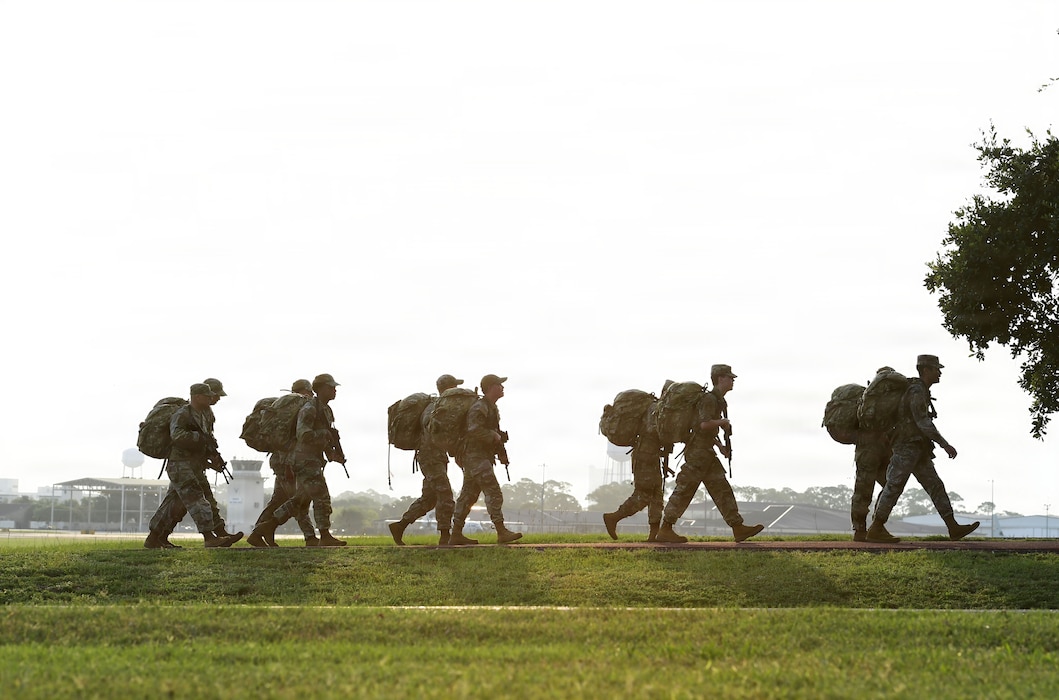 A group of people wearing U.S. Air Force military uniforms march in formation while carrying ruck sacks.