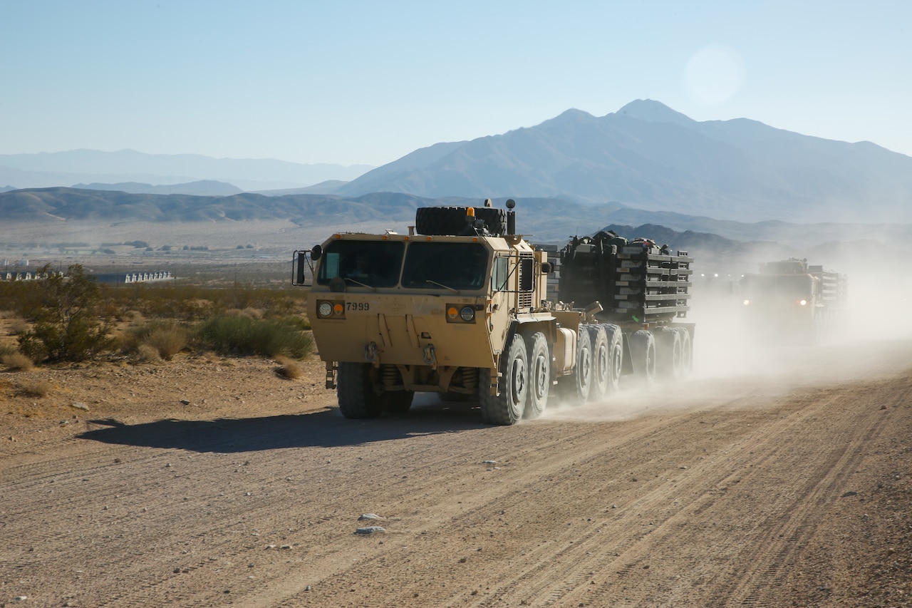 A convoy of military trucks in motion along a dirt highway during daytime.