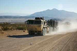 A convoy of military trucks in motion along a dirt highway during daytime.