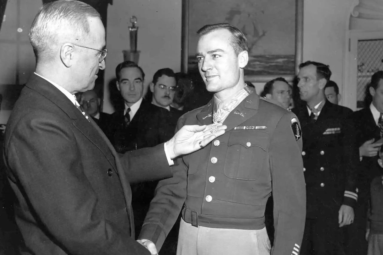 A man wearing business attire shakes hands with a man in a formal military uniform.