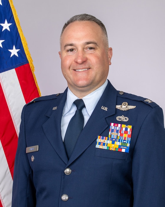 Male officer in dress blue Air Force uniform with American flag behind right shoulder