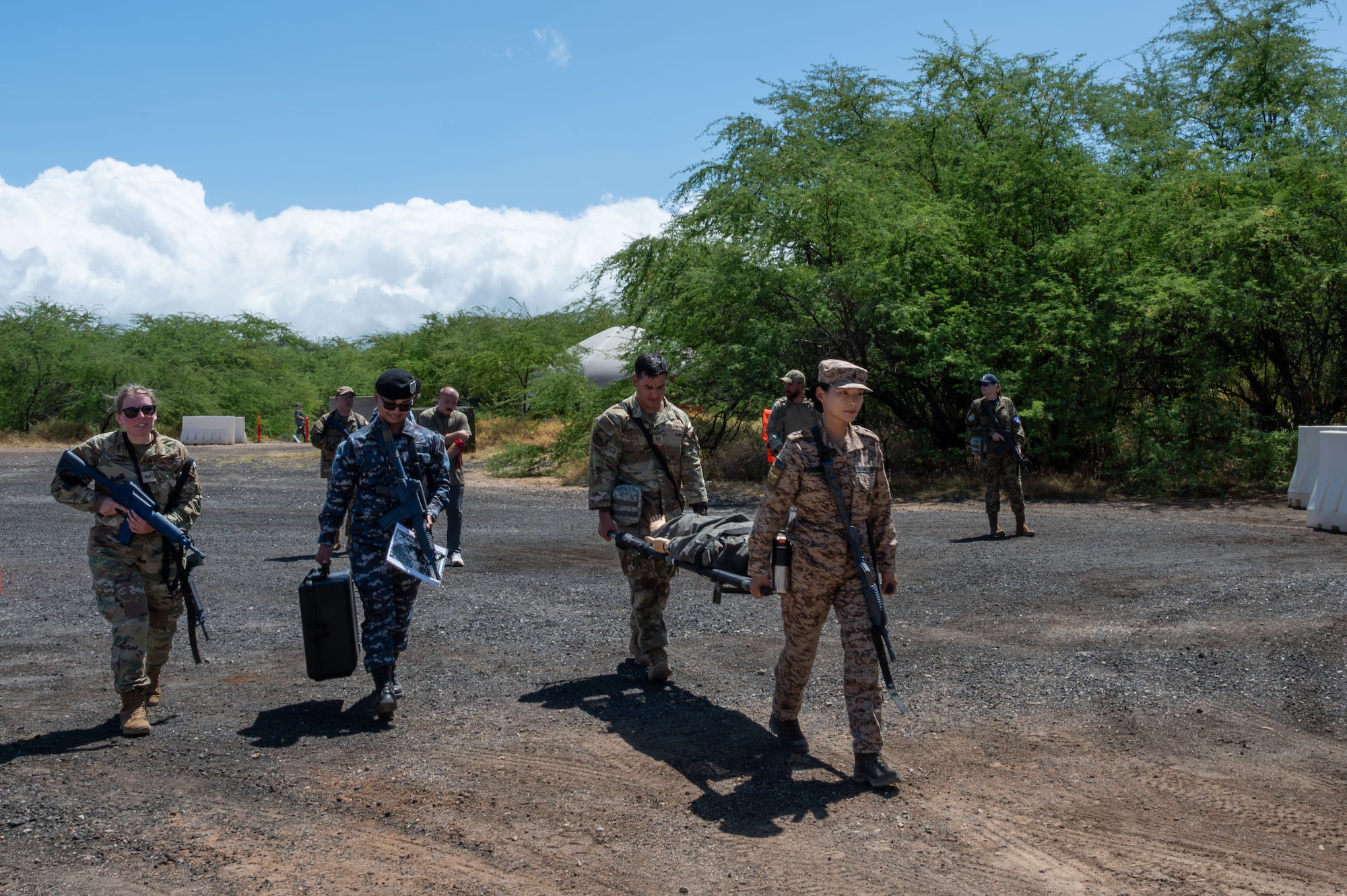 Multinational airmen are carrying a gurney across a concrete pad