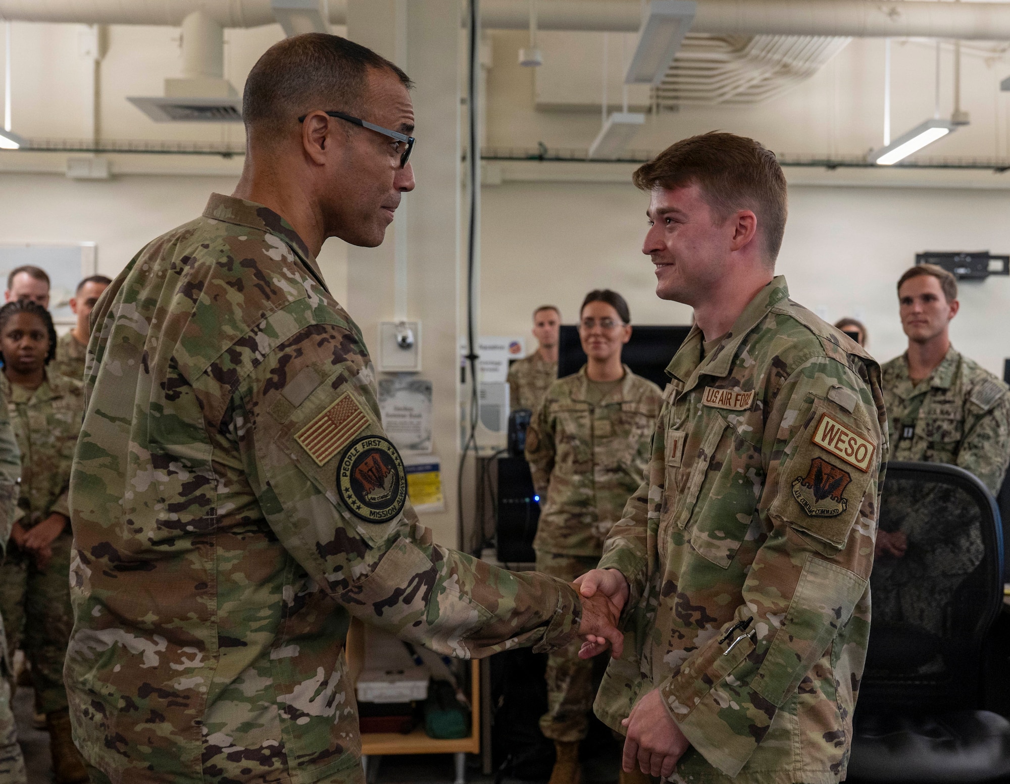 U.S. Air Force Gen. Adrian Spain coins 2nd Lt. Chase Purdy as they shake hands in an operations center while other service members look on.