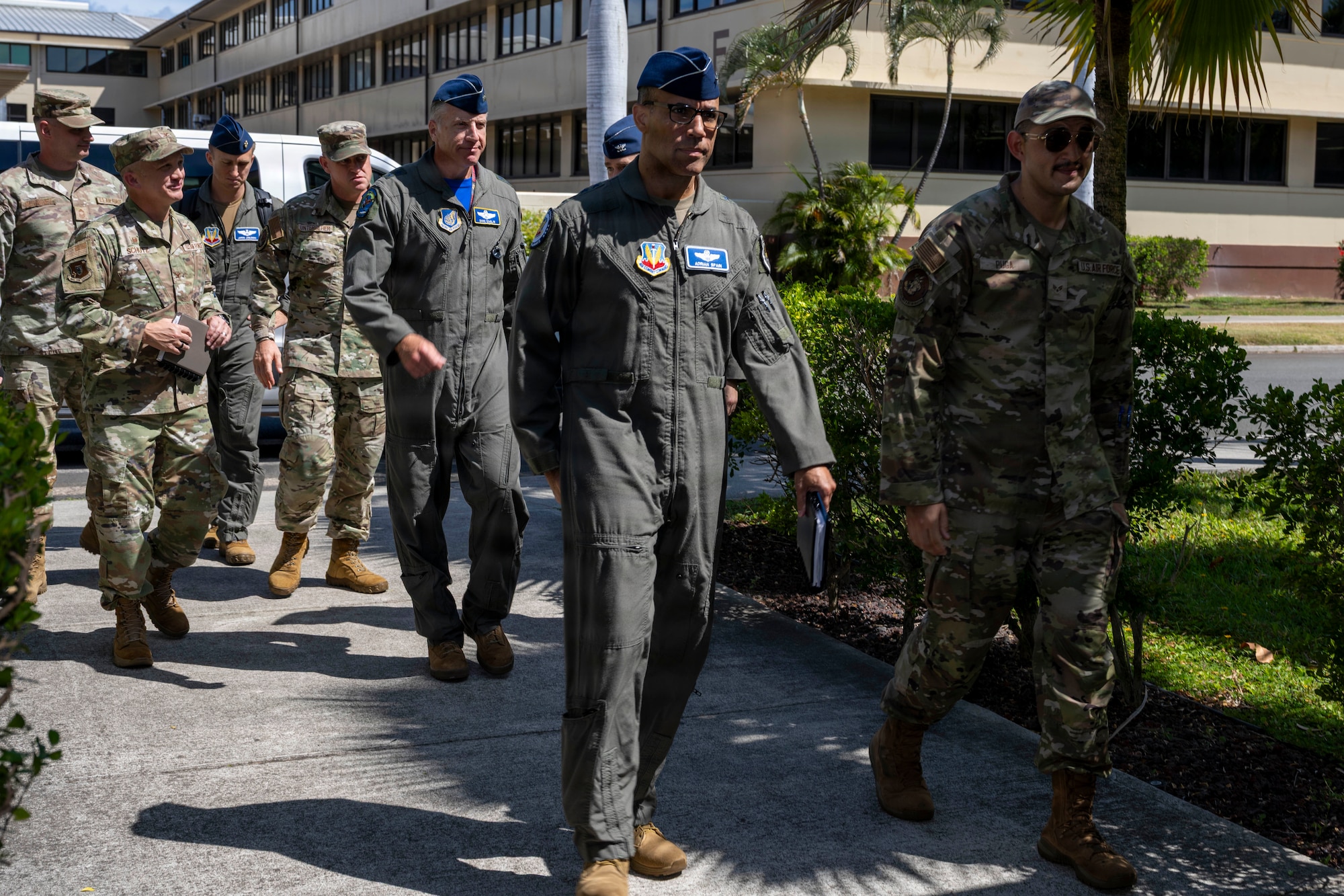 U.S. Air Force Gen. Adrian Spain walks with a group of Airmen outdoors on a paved walkway in front of a building. The group wears a mix of green flight suits and camouflage uniforms.