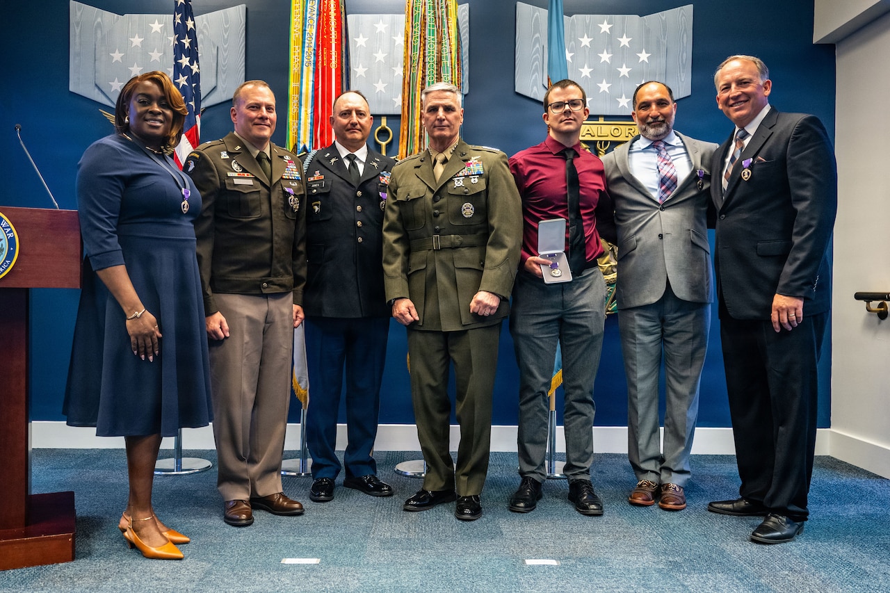 A Marine Corps general stands with six service members and civilians wearing or holding Purple Heart medals.