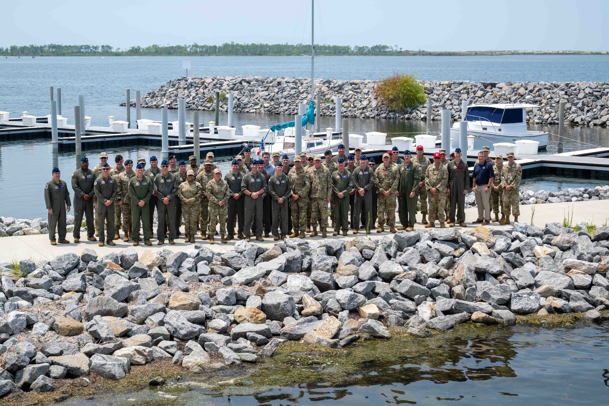 A group of roughly 60 military members pose for a photo at a marina