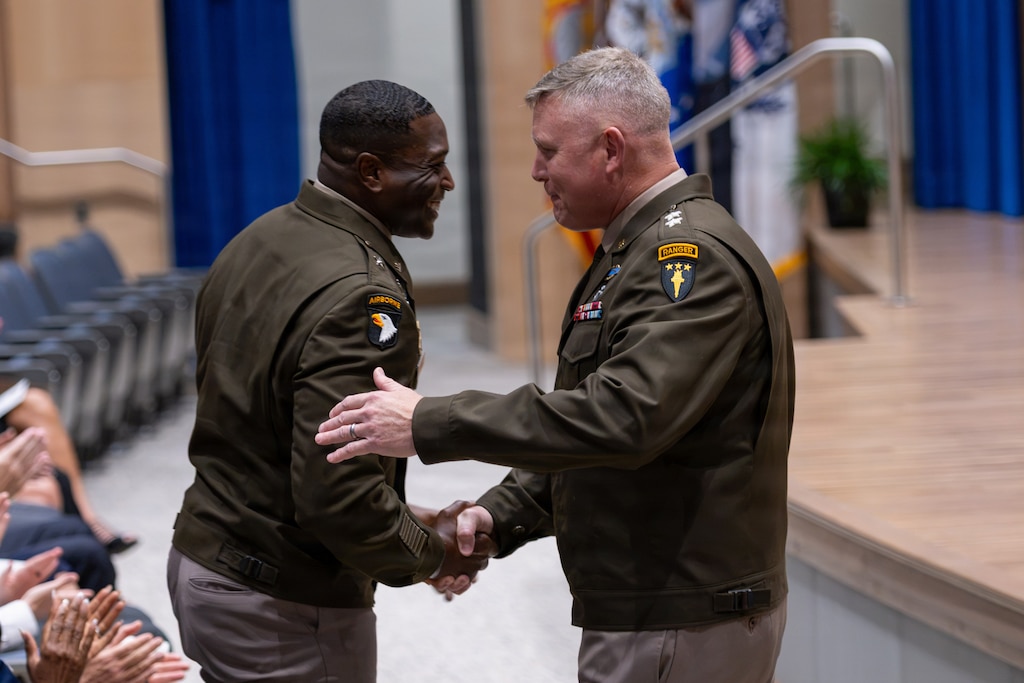 Two Army officers in Army Green Service Uniforms (AGSUs) share a firm handshake during an official ceremony.