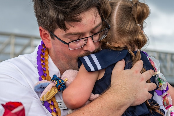 A close-up of a man in a camouflage military uniform hugging a young girl.