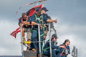 Six people in military uniforms and casual attire stand on top of a submarine as they signal to other people.