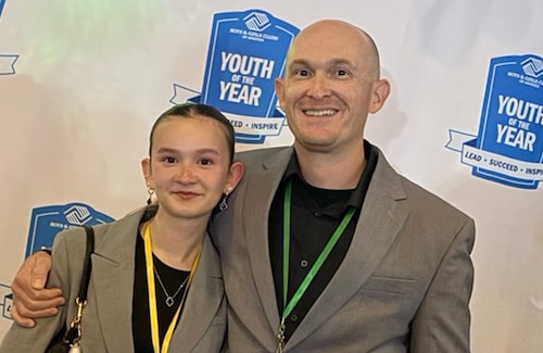 Daughter and Guardian pose in front of an award wall.
