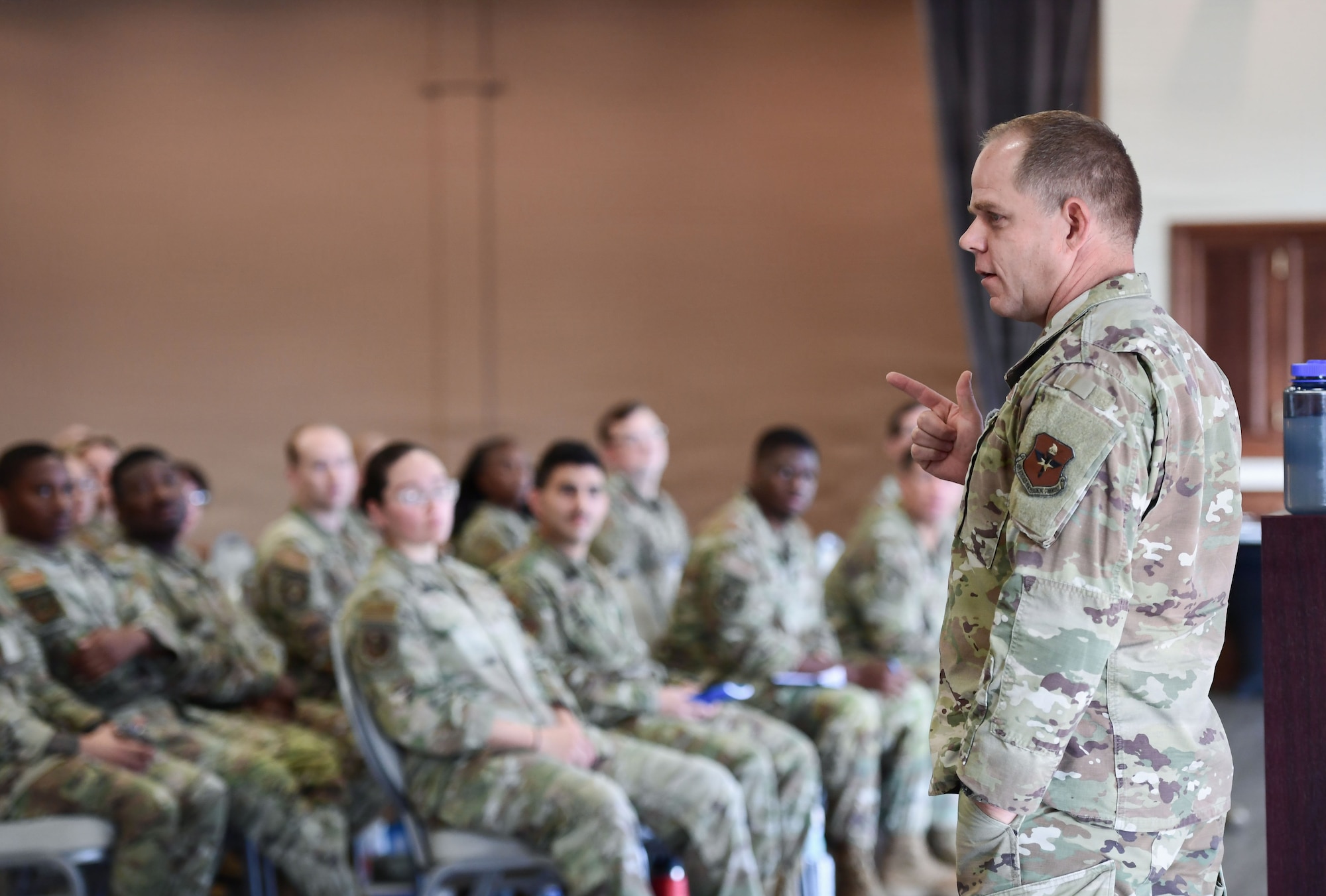 A man in a U.S. Air Force uniform speaks to a crowd of Airmen.