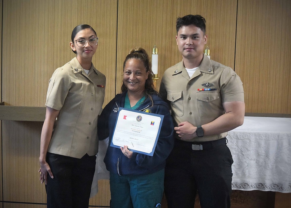 Navy Medicine Training Support Center (NMTSC), Detachment Camp Lejeune held a ceremony on July 23, 2026, honoring its latest students from the Surgical Technology Program (Phase II) graduates Hospital Corpsman Second Class Emely Betancourt (left) and Hospital Corpsman Second Class Caue Uemura (right) present civilian surgical technologist Azucena Naval with Naval Medical Center Camp Lejeune the “Golden Scalpel Award.” The award honors the preceptor the surgical technology students feel most assisted with their development in the course.