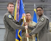 photo of three Airmen standing on a stage, two Airmen are holding a unit flag in between them