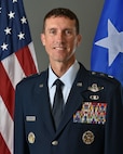 General Epperson poses for an official photo with a grey background with the U.S. flag on the left and a white star with blue background flag on the right.