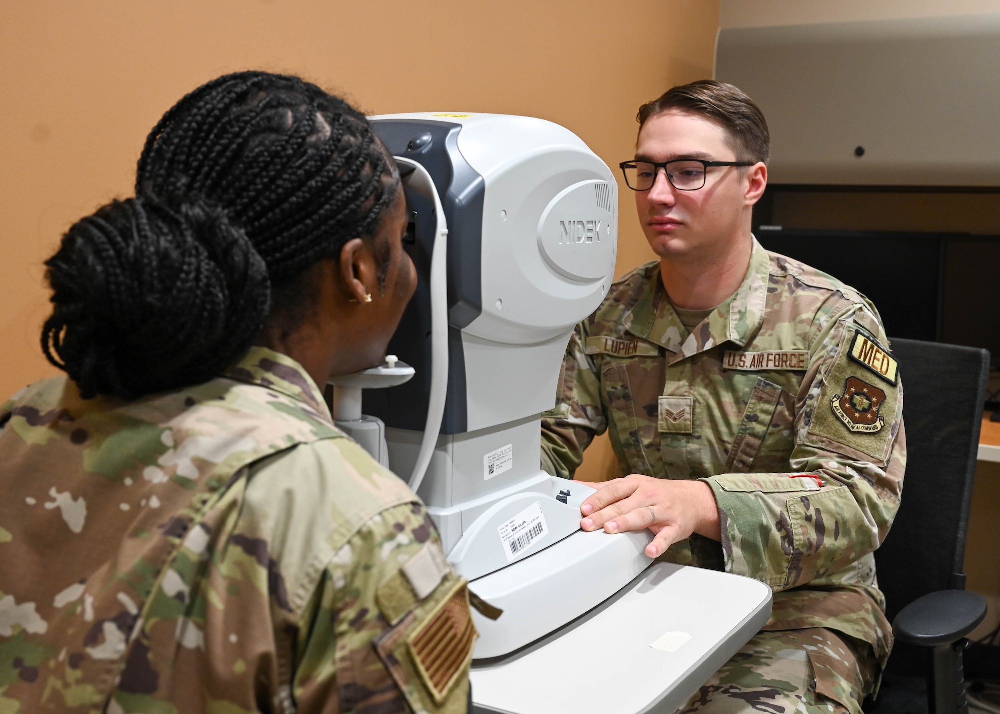 U.S. Air Force Senior Airman Wyatt Lupien, right, Luke Medical Group Operational Medical Readiness Squadron optometry technician, operates an autorefractor during an eye exam at Luke Air Force Base, Arizona, July 29, 2026. Through routine emergency medical training and certification, Air Force medical personnel develop the confidence and skills needed to respond effectively when lives are on the line, both on and off duty.
